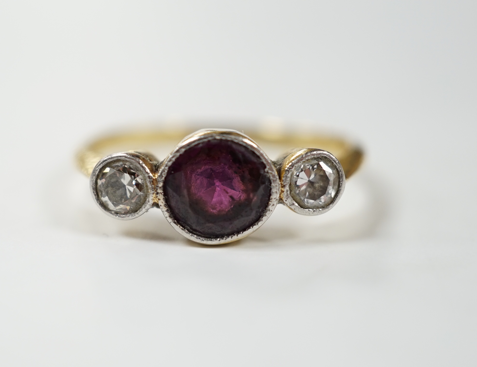 An early 20th century yellow metal and millegrain set single stone garnet and two stone diamond ring, size M, gross weight 2.8 grams.